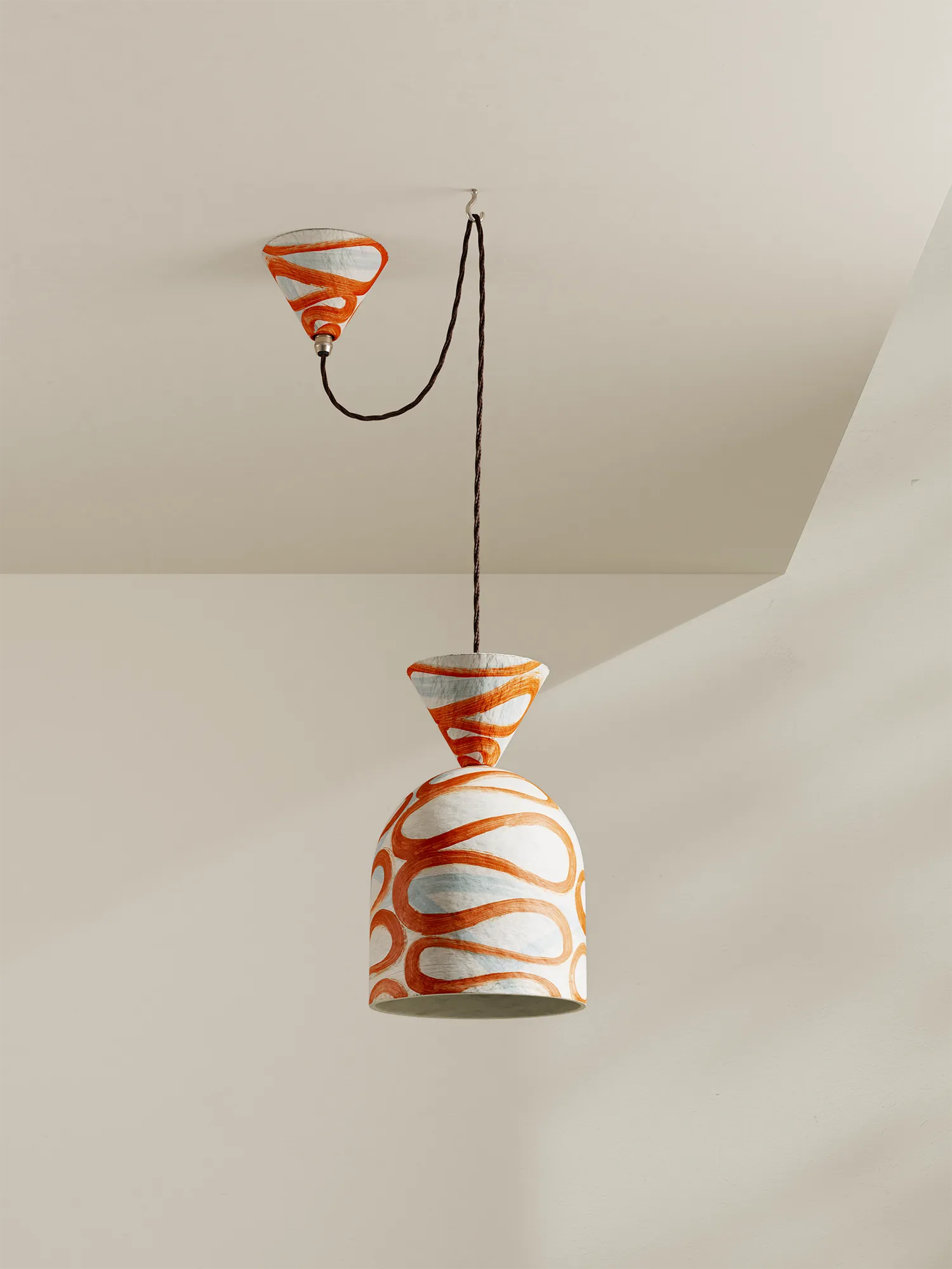 A paper-pilp pendant light with brick-orange and white design on a neutral background