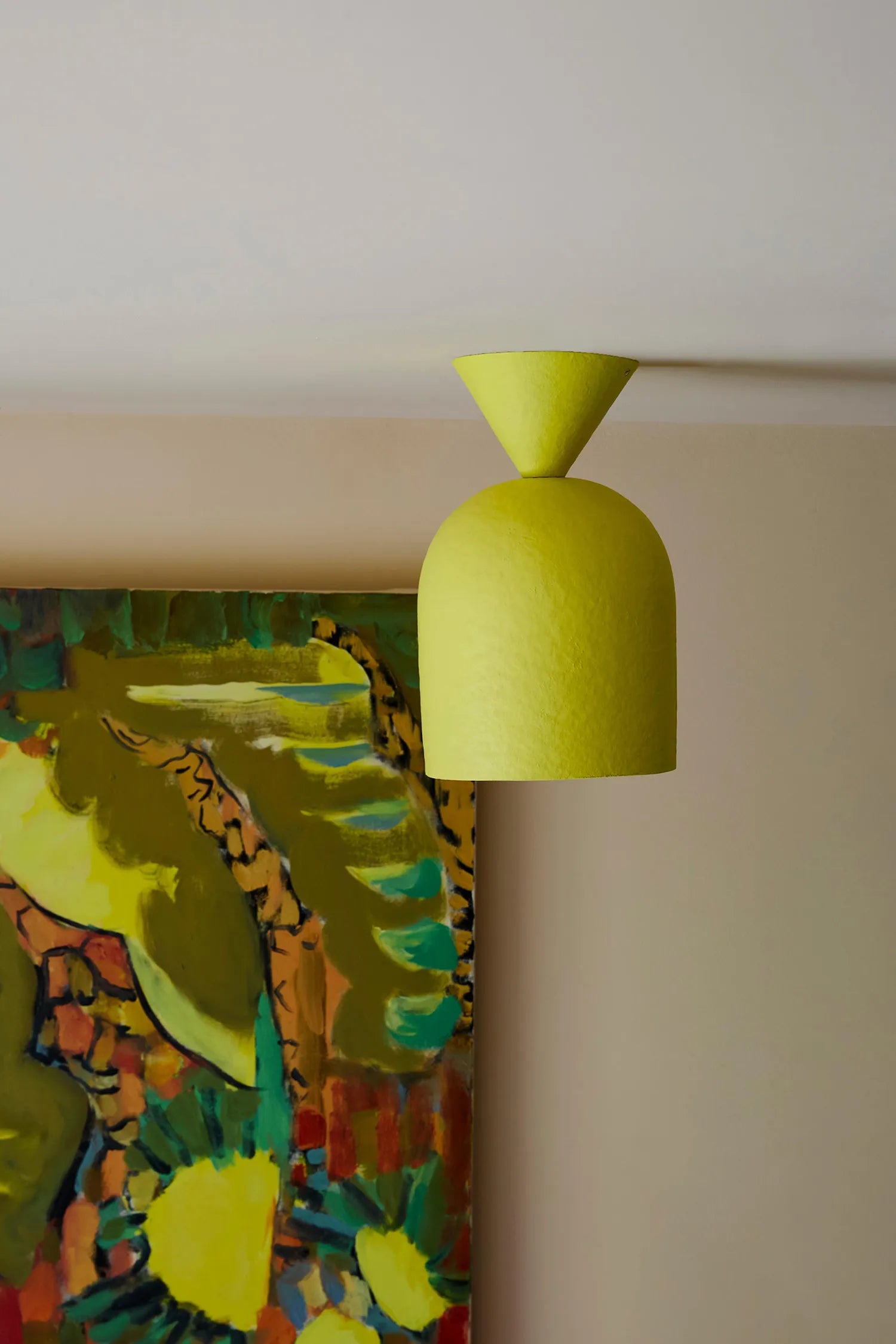 A bright yellow dome light with a conical top, shown suspended against a beige wall next to a colorful abstract painting.