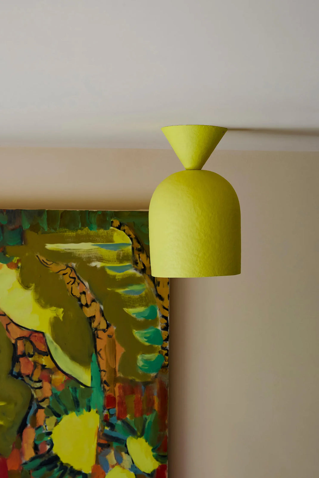 A bright yellow dome light with a conical top, shown suspended against a beige wall next to a colorful abstract painting.