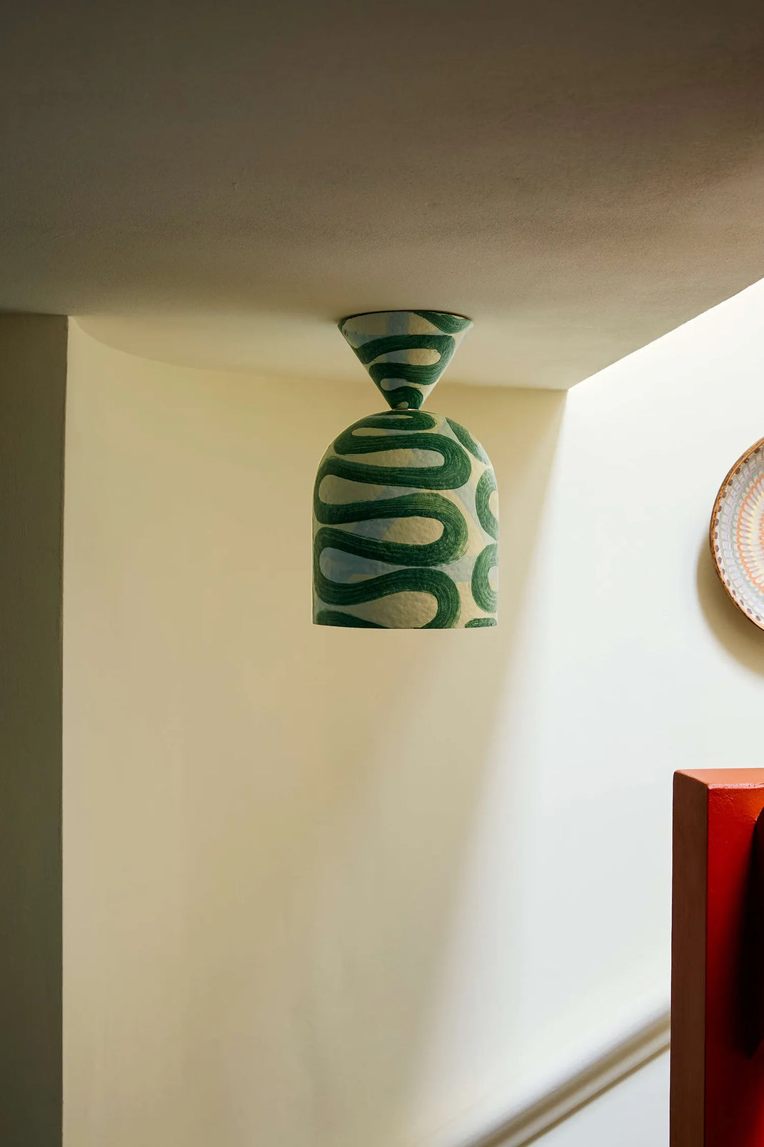 Surface mount light with green wavy pattern hanging from a white ceiling