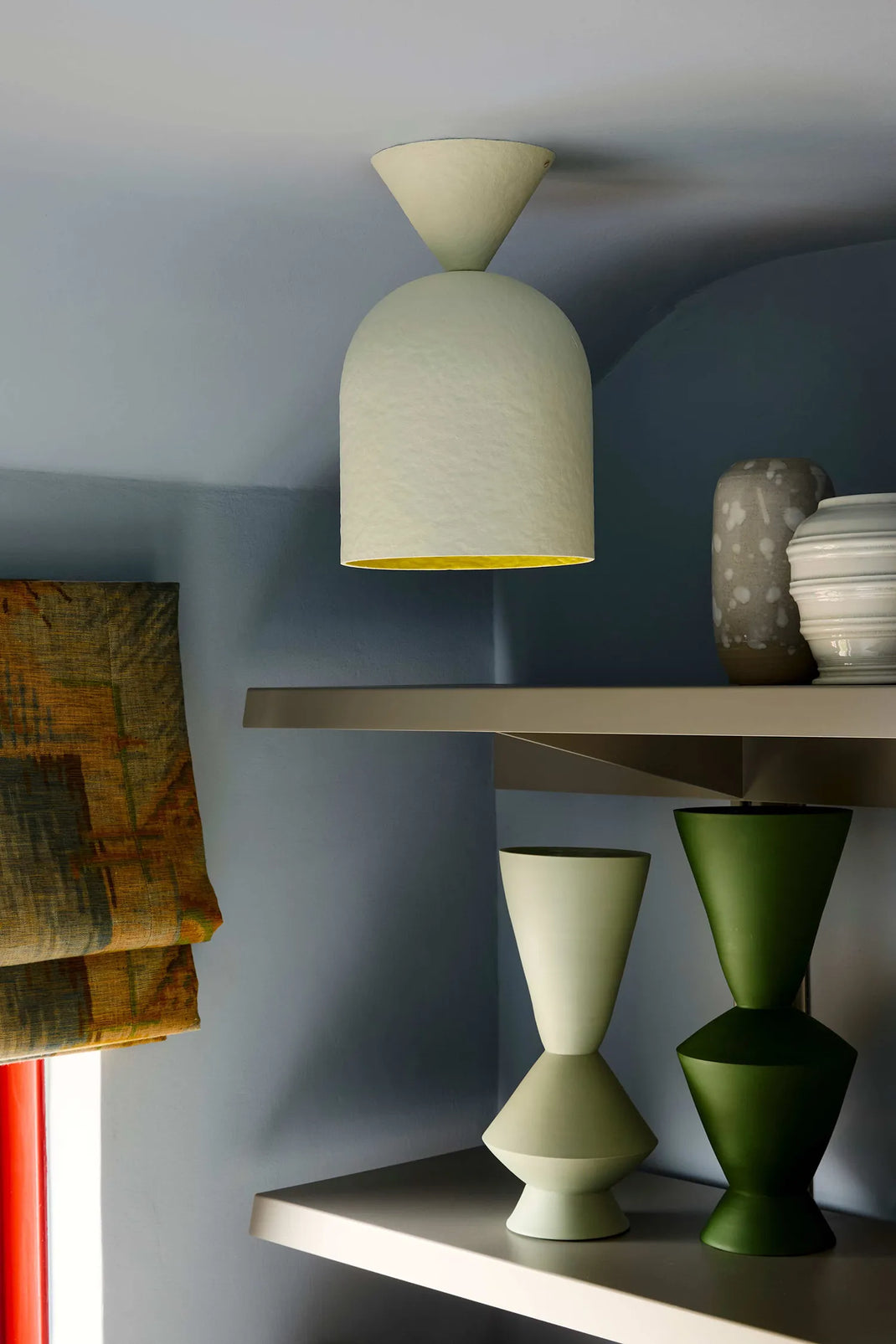 A modern surface mount light with a textured off-white dome shade and a yellow interior, mounted on a light gray ceiling above floating shelves with ceramic vases.