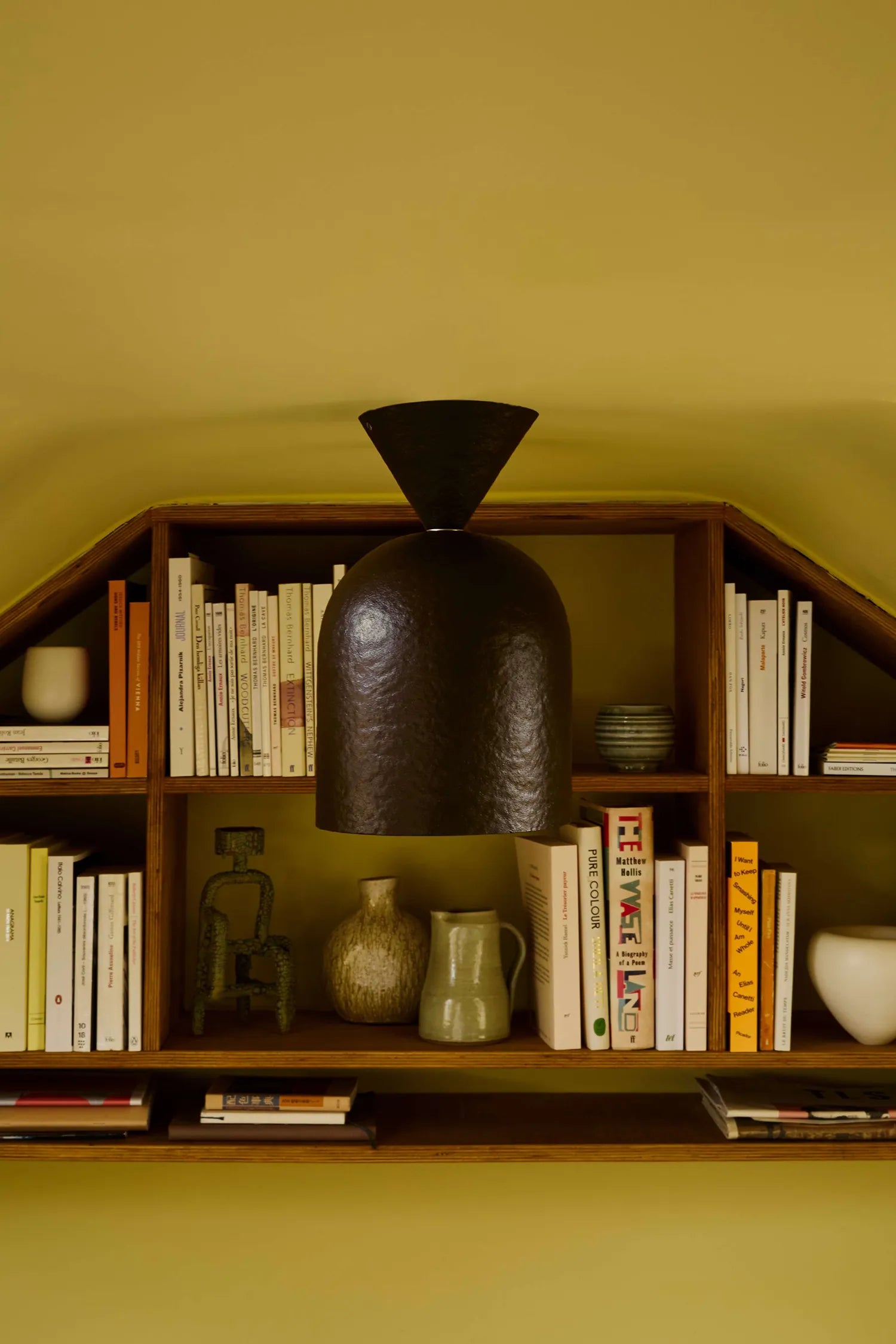 Dark brown ceiling light against a wooden shelf with books and decorative items and a yellow wall.