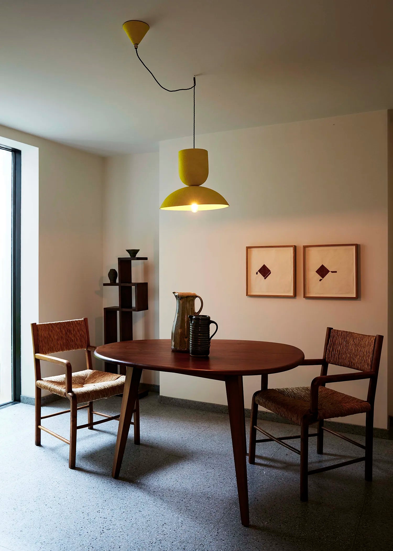 Dining room with wooden table and chairs, yellow pendant light, and framed artwork on the wall.