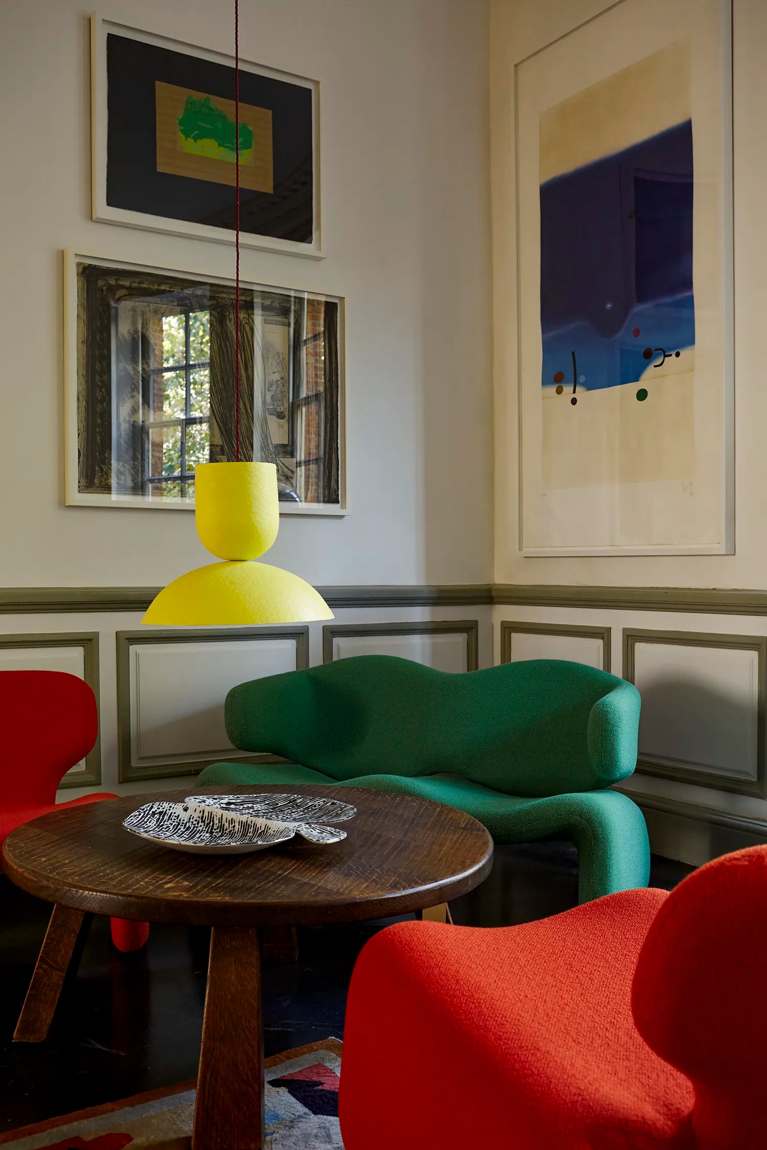 Modern interior with yellow pendant, colorful chairs, a round wooden table, and abstract art on the walls.