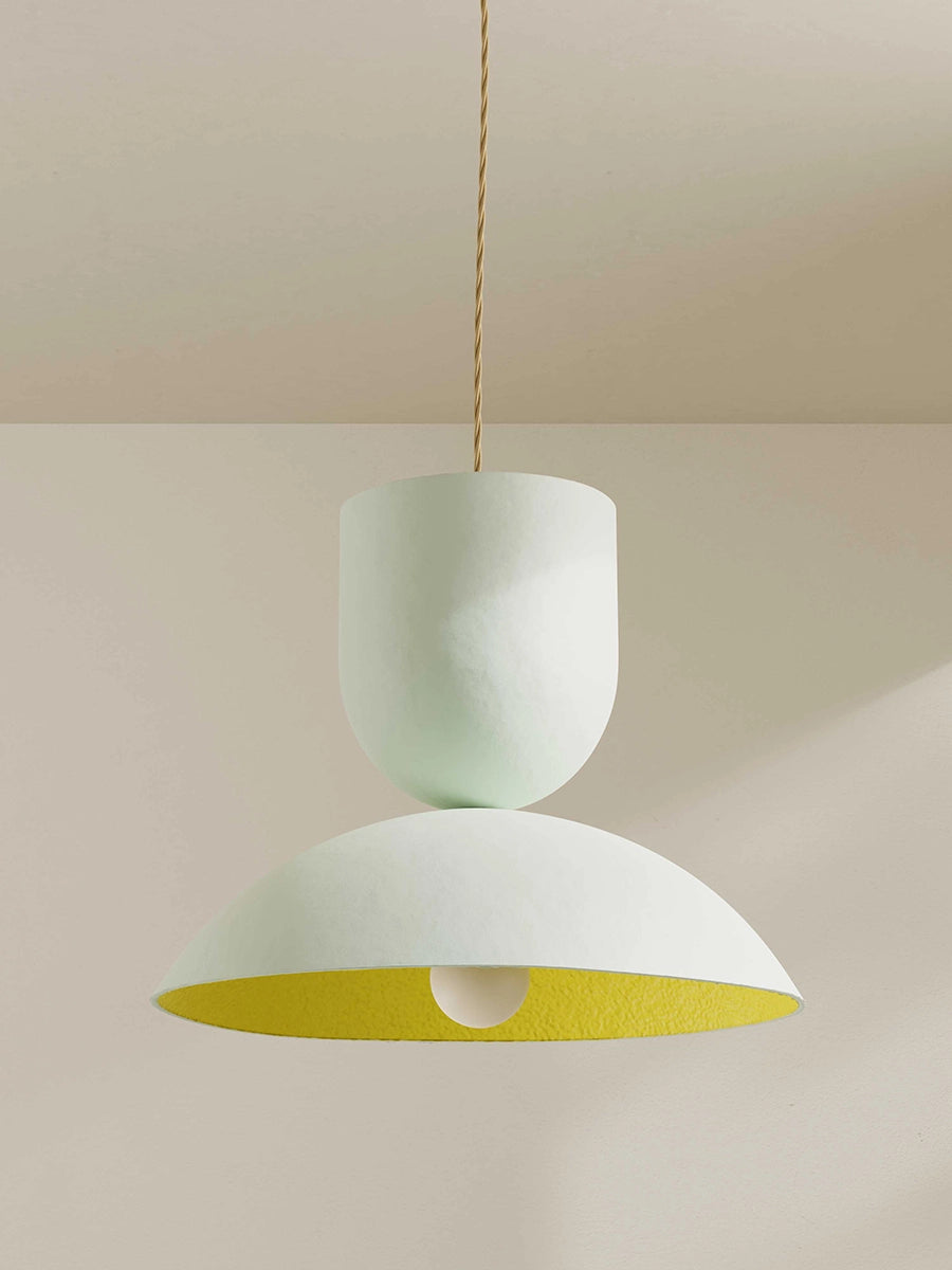 Pendant light with white top and yellow bottom on a neutral background