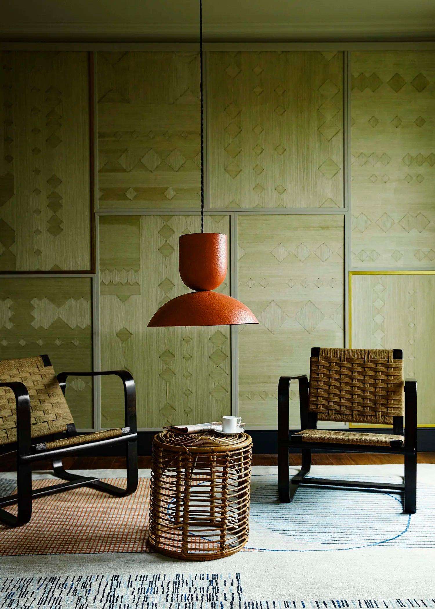 Living room with patterned wall, wooden chairs, and a pendant lamp.