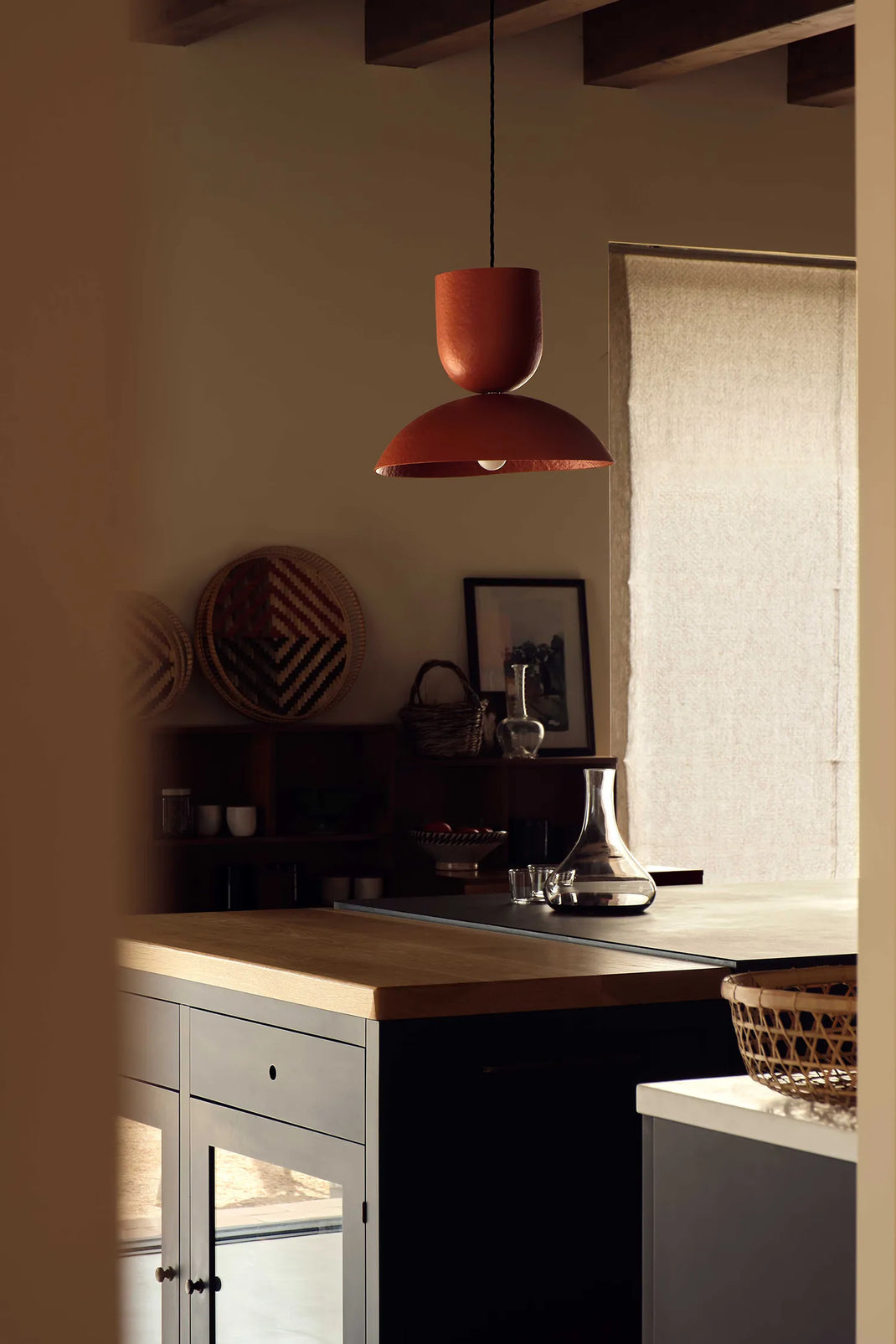 Modern kitchen interior with a red pendant light, wooden countertop, and gray cabinets.