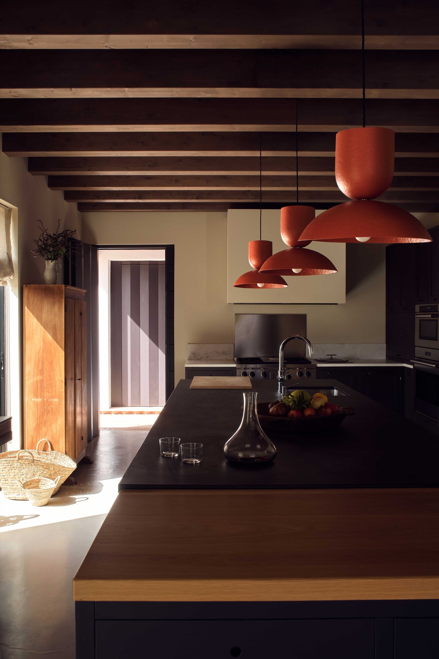 Three orange/red hand-painted Buoy pendants over a kitchen island, made from paper pulp.