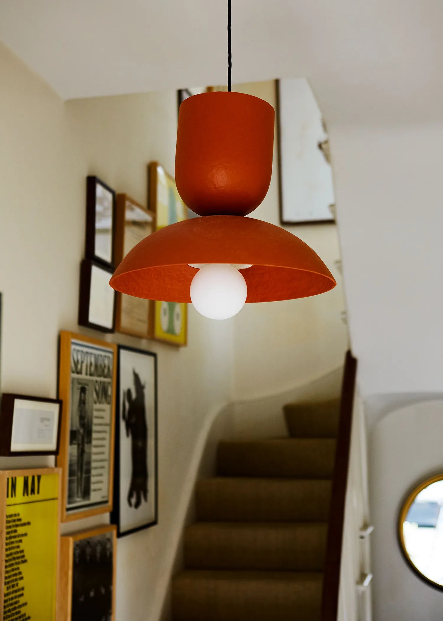 Red pendant light hanging in a hallway with framed pictures on the wall and a staircase.