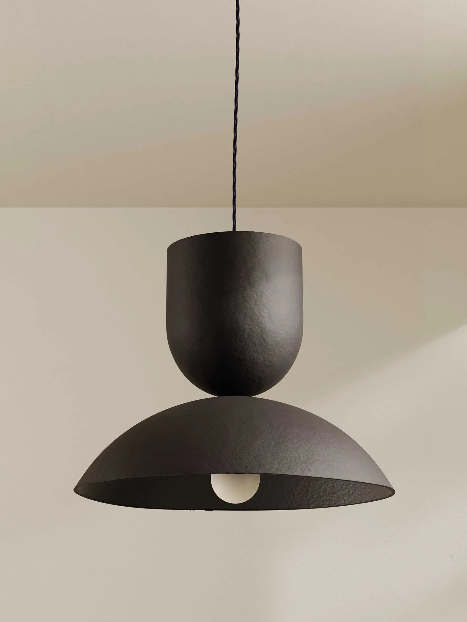Brown-black pendant light hanging against a neutral background