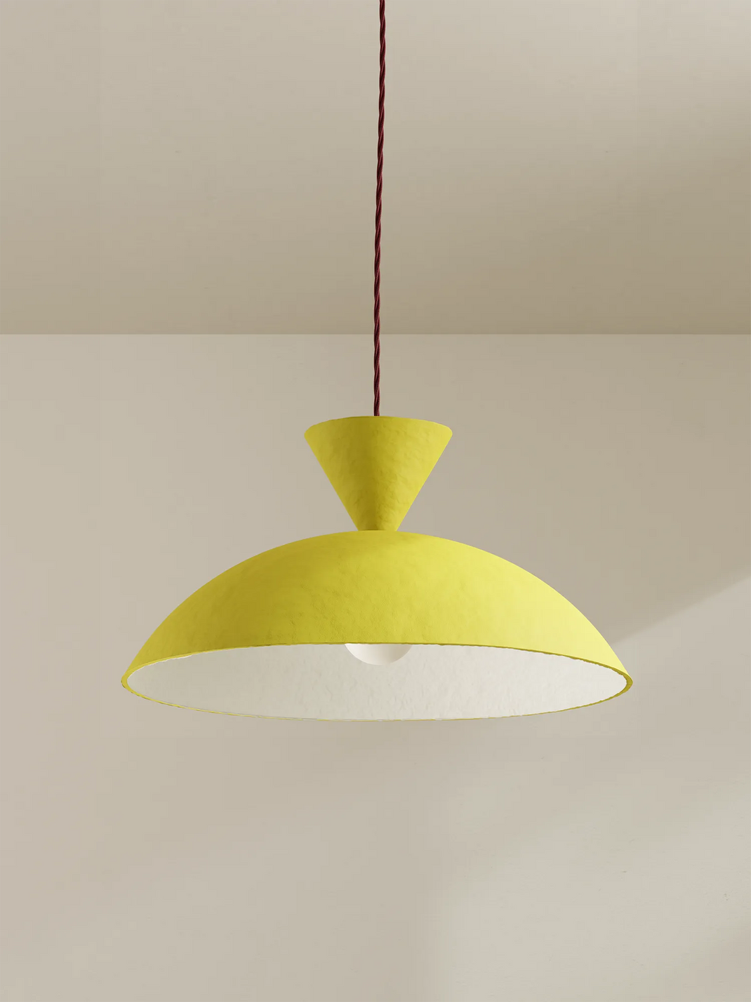 A modern pendant light with a textured yellow dome shade and a conical neck, suspended by a burgundy cord against a minimalist beige wall and ceiling.
