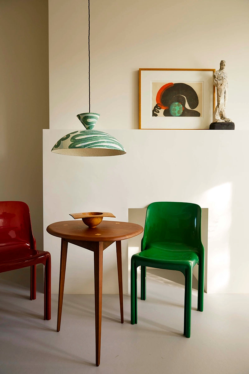 Modern interior with a wooden table, green chair, and red chair under a pendant light.