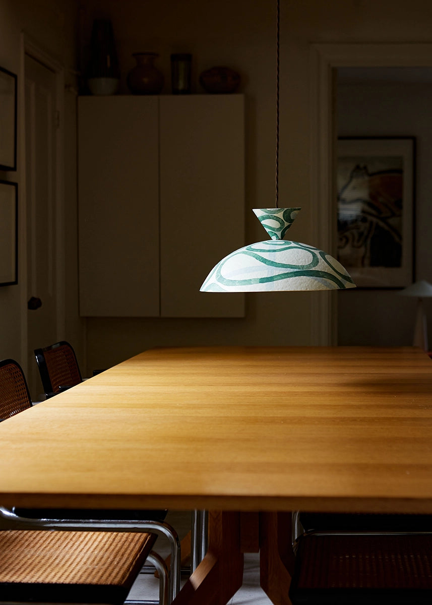 Dining room with a wooden table and a pendant lamp with green and white pattern.