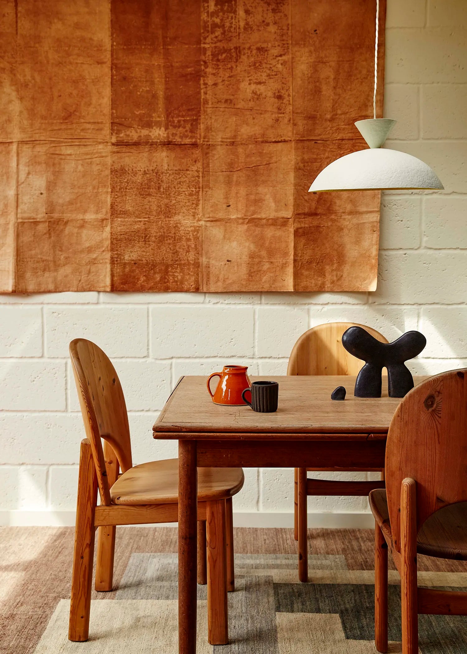 Dining area with wooden table and a white pendant hanging above against a textured wall