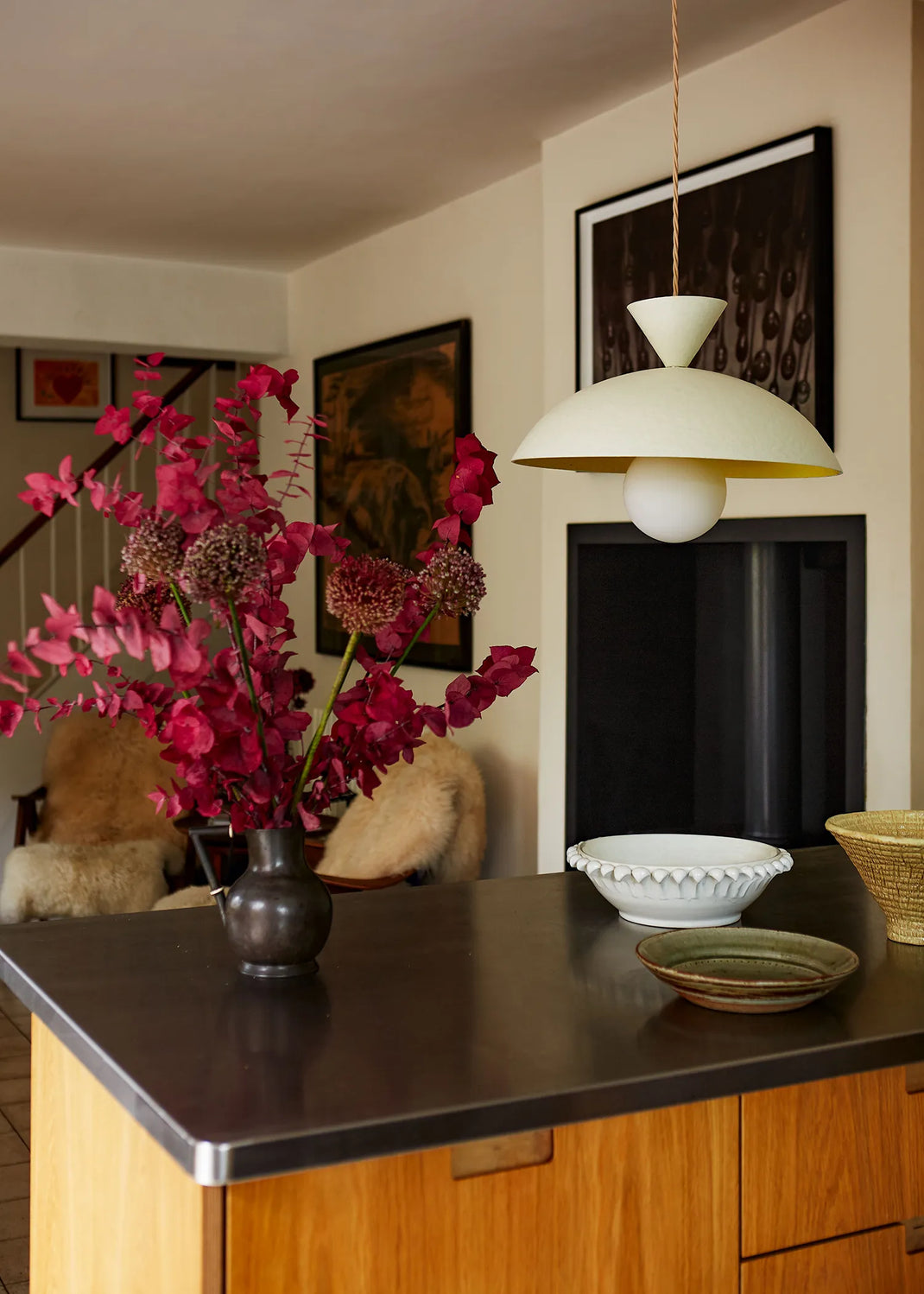 Floral arrangement on a kitchen counter with a pendant light and framed pictures in the background.
