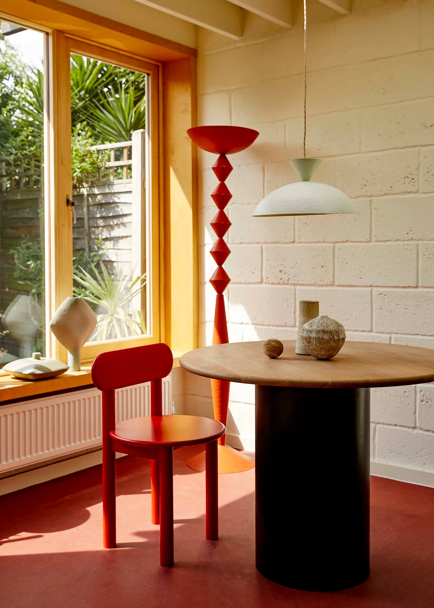 Modern interior with a red chair, round table, and geometric lamp.