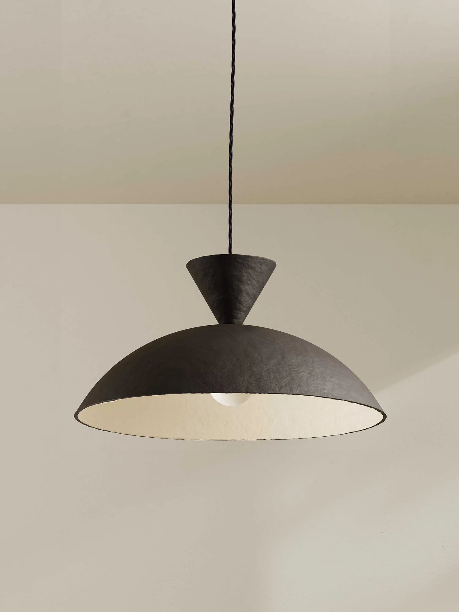 A modern pendant light with a textured brown-black dome shade, a warm cream-colored interior, and a dark blue hanging cord, shown against a minimalist beige wall and ceiling.