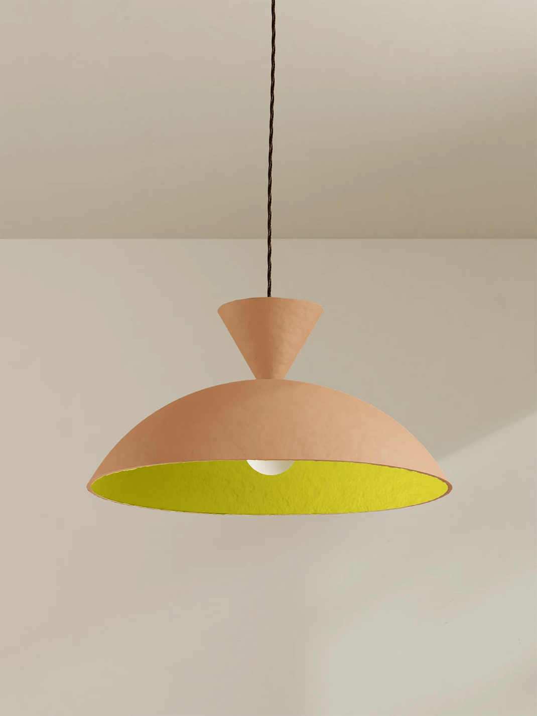 Peach coloured pendant light with a bright yellow interior against a minimalist background.