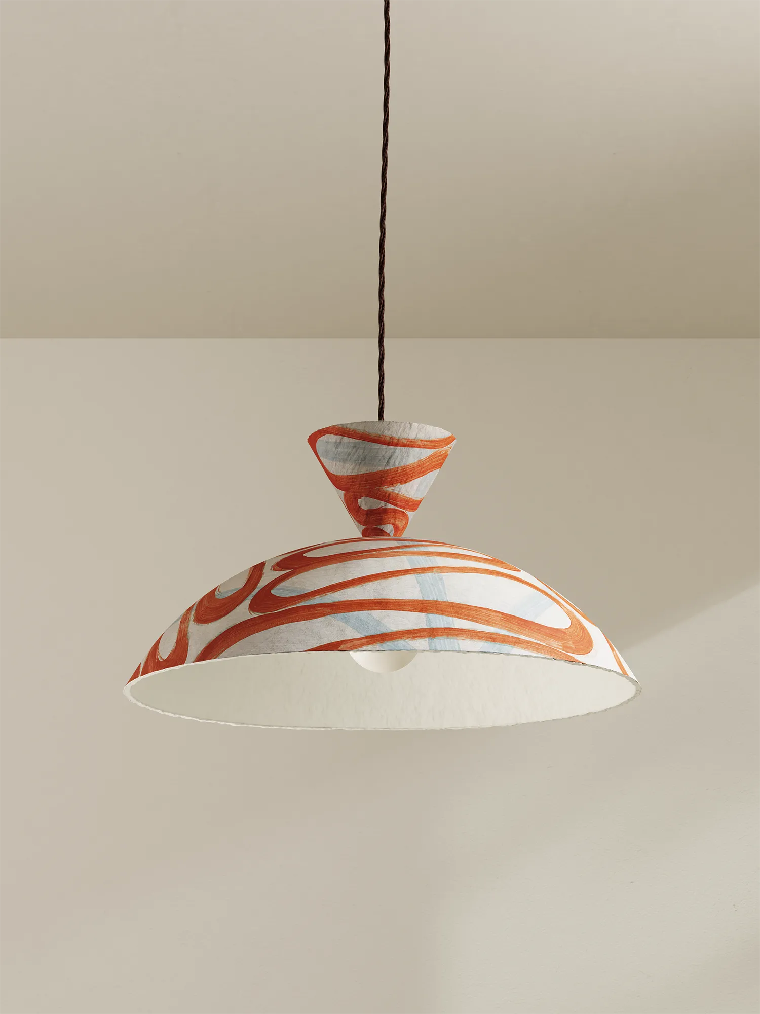 A modern pendant light with a wide, shallow dome shade featuring a white and orange marbled pattern, suspended by a brown cord against a neutral beige wall and ceiling.