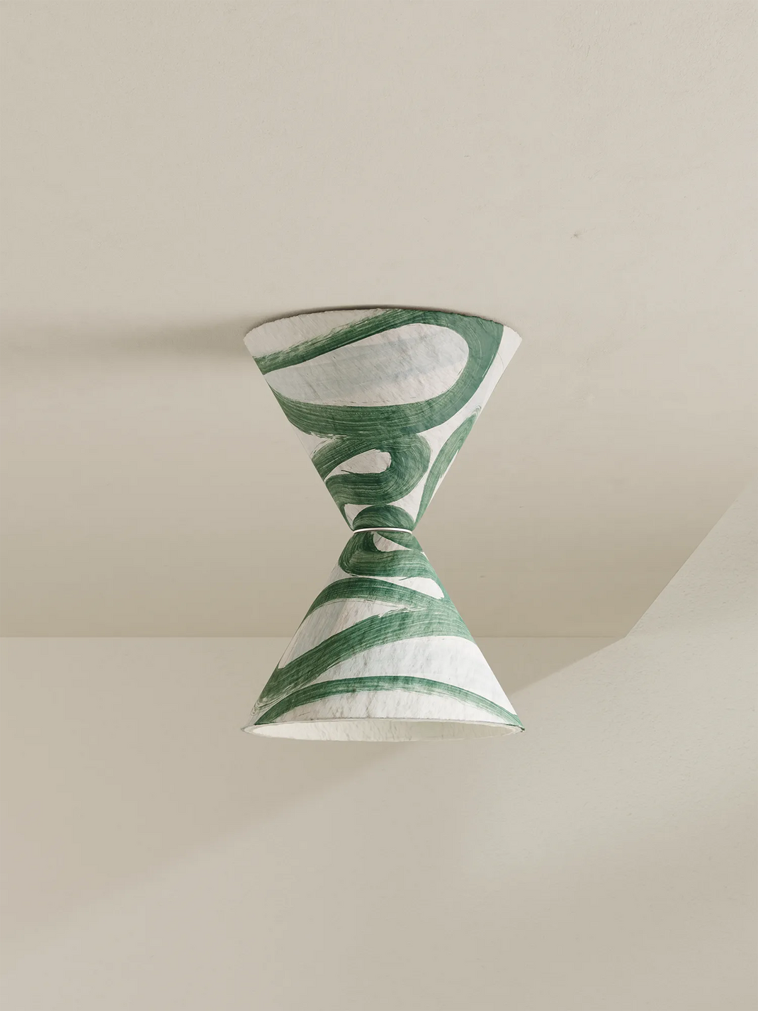 A modern hourglass-shaped ceiling light with a green and white abstract patterned shade, suspended against a minimalist beige wall and ceiling.