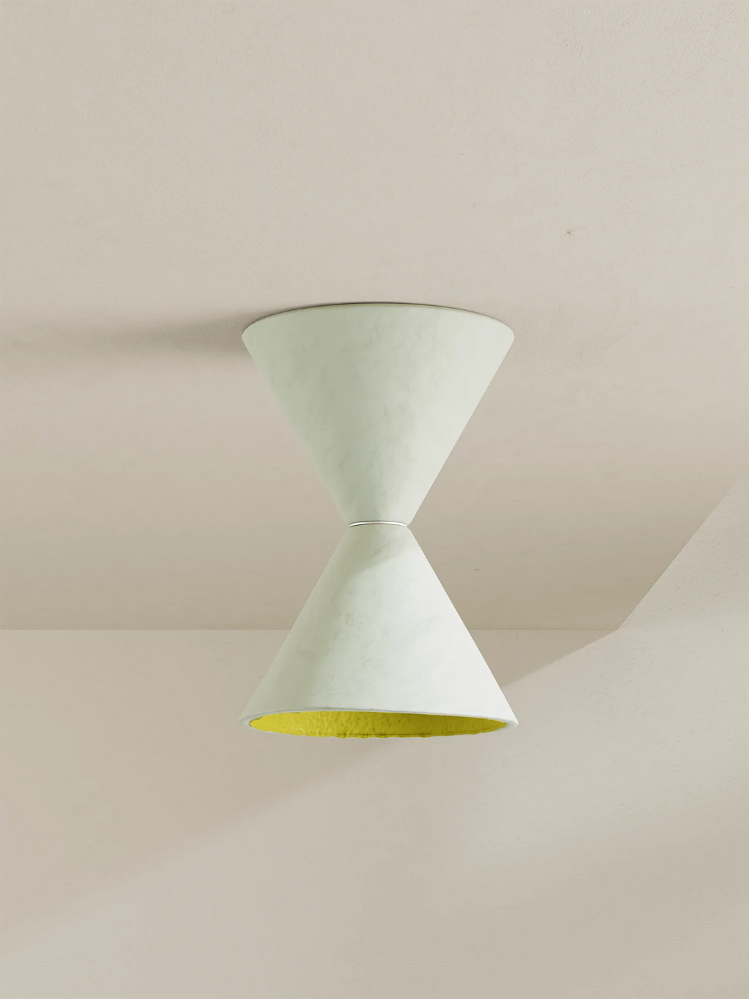 A modern geometric ceiling light fixture with two conical shades meeting at a center band, shown against a warm beige plaster ceiling and wall. The outer shade is a white with a hint of mint, and the inner shade is a bright chartreuse yellow.
