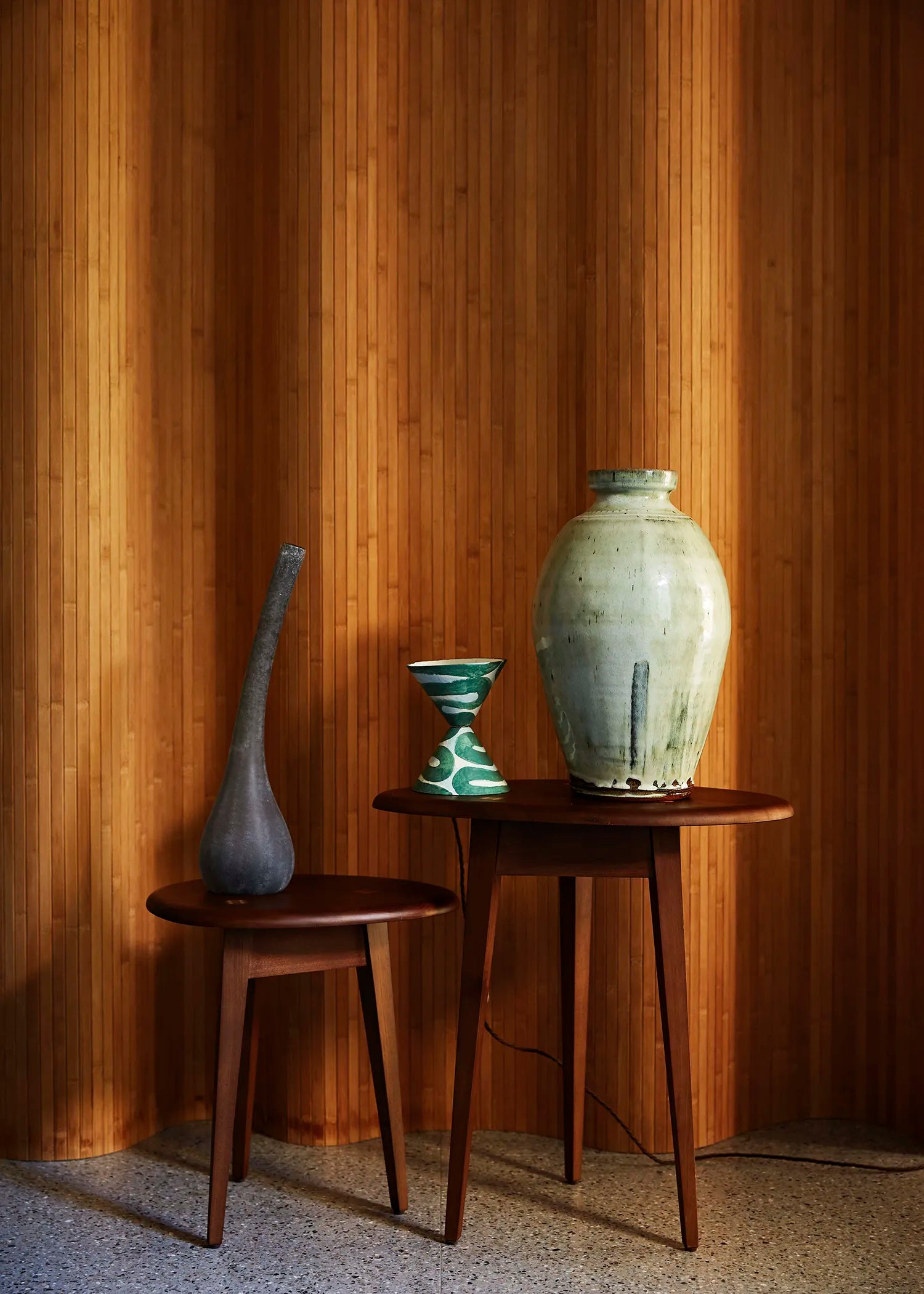 Two mid-century modern wooden side tables with tapered legs, styled with a green and white table lamp against a vertical wood-paneled screen.