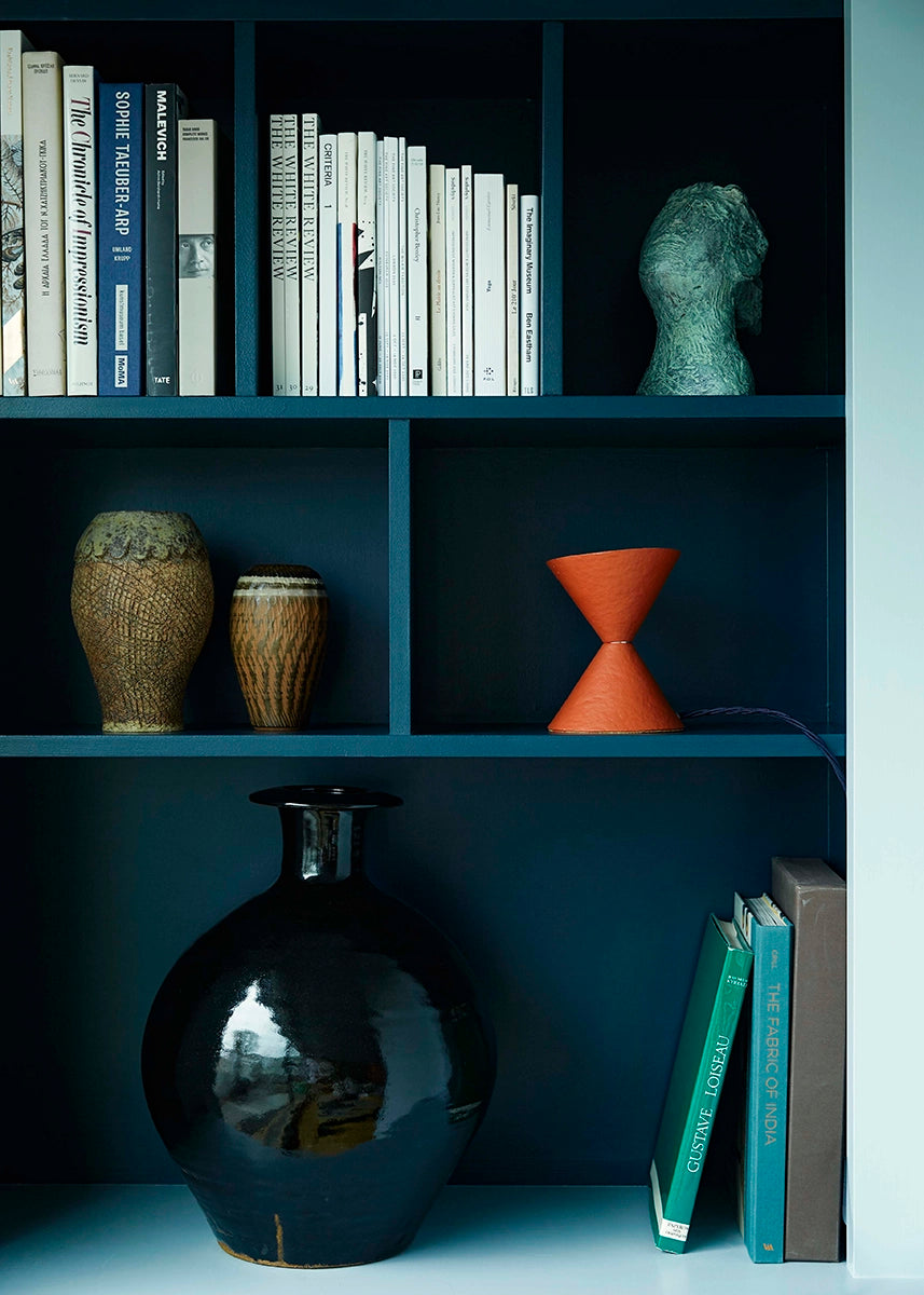 Small uplighter in brick red on a blue shelf.