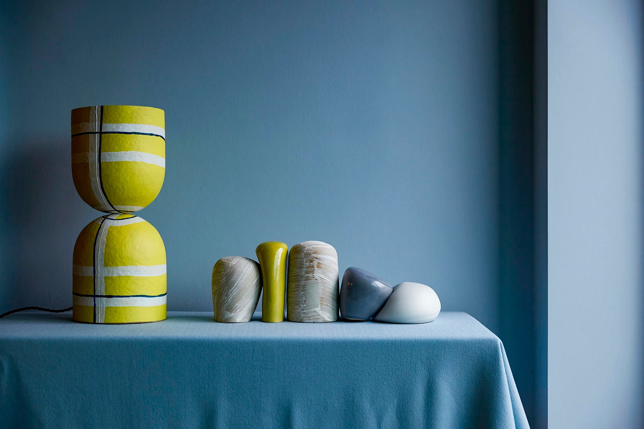 A yellow and white patterned table lamp on a table with ceramic pebbles.