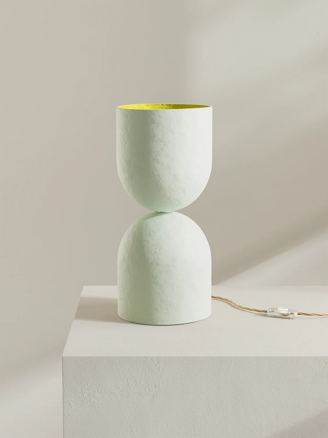 Two-tiered ceramic lamp on a white pedestal against a beige background