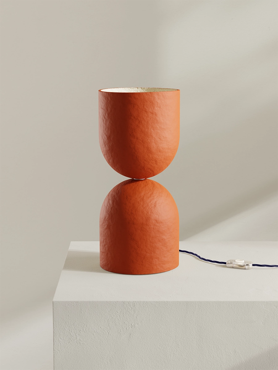Brick orange table lamp with a textured design on a white pedestal against a light gray background