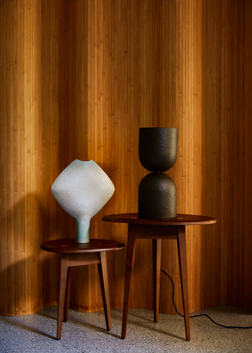 Two wooden side tables with a dark brown table lamp against a wooden paneled wall.
