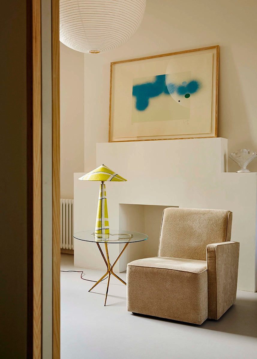 Modern living room with beige armchair,  yellow geometric lamp, glass table, and abstract painting on the wall.