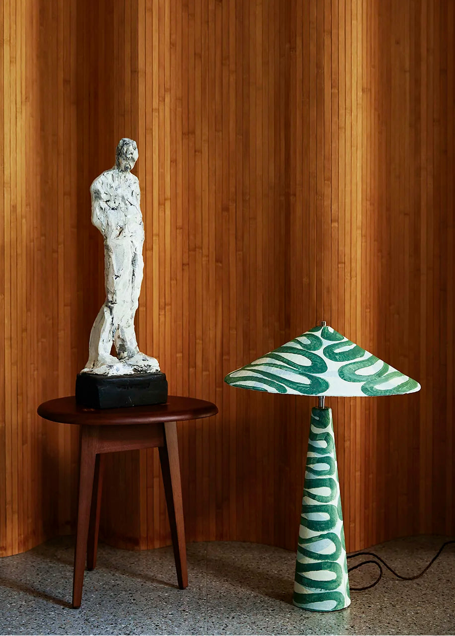 White marble sculpture on a wooden table with a green and white patterned lamp against a wooden paneled wall.