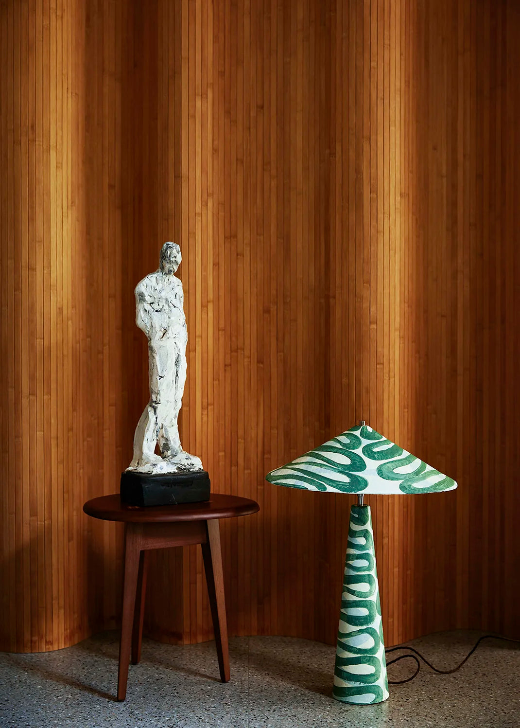 White marble sculpture on a wooden table with a green and white patterned lamp against a wooden paneled wall.