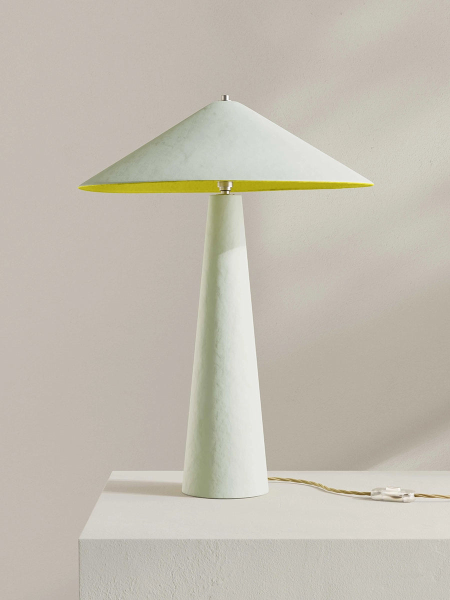 Table lamp with a white base and greenish-yellow conical shade on a light gray background