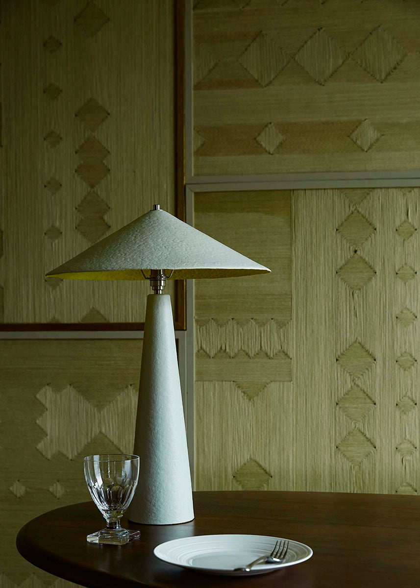 Table lamp on a table with a plate and glass against a patterned wall.