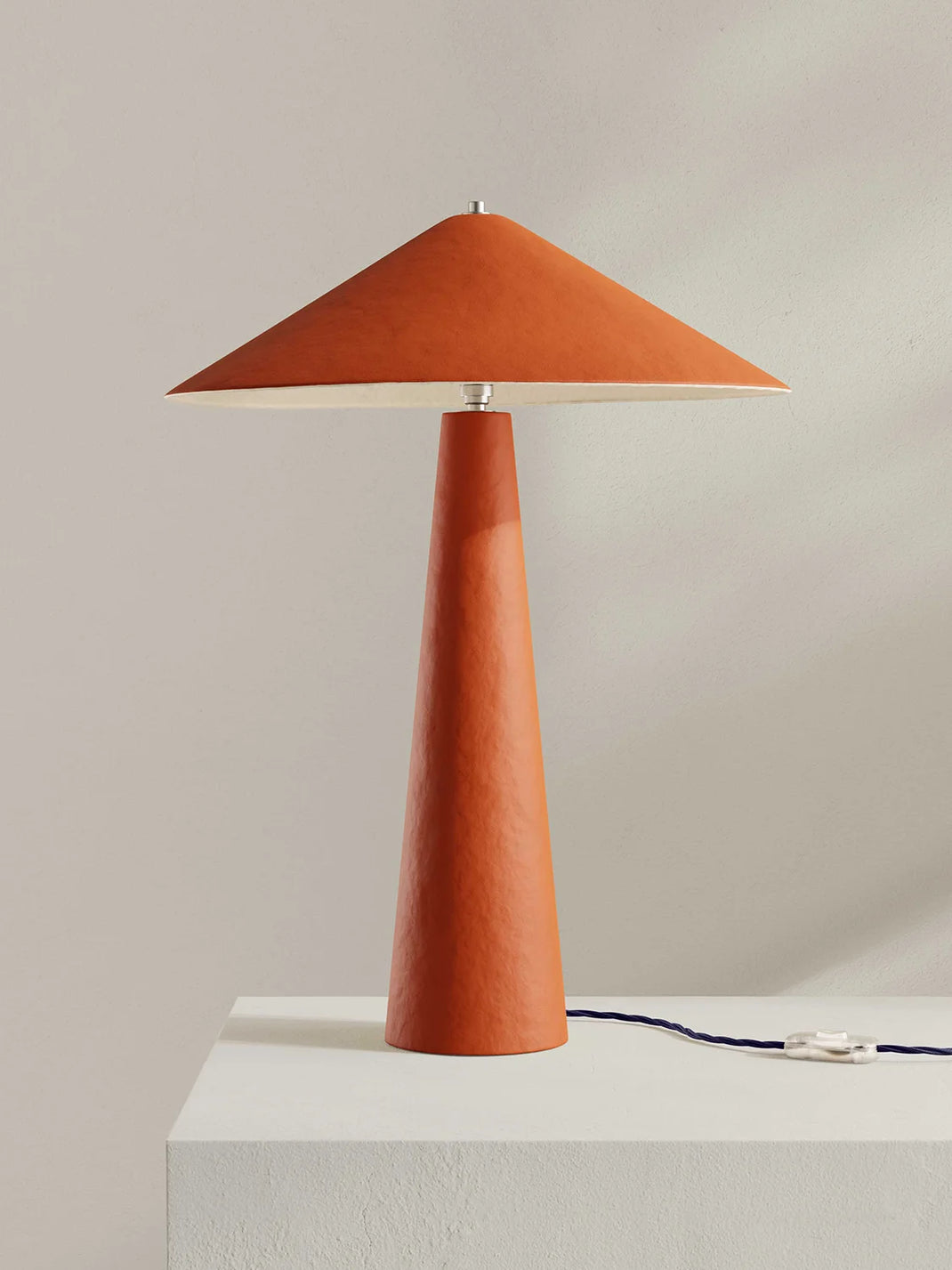 Orange table lamp with a conical base and pyramid-shaped shade on a light gray background