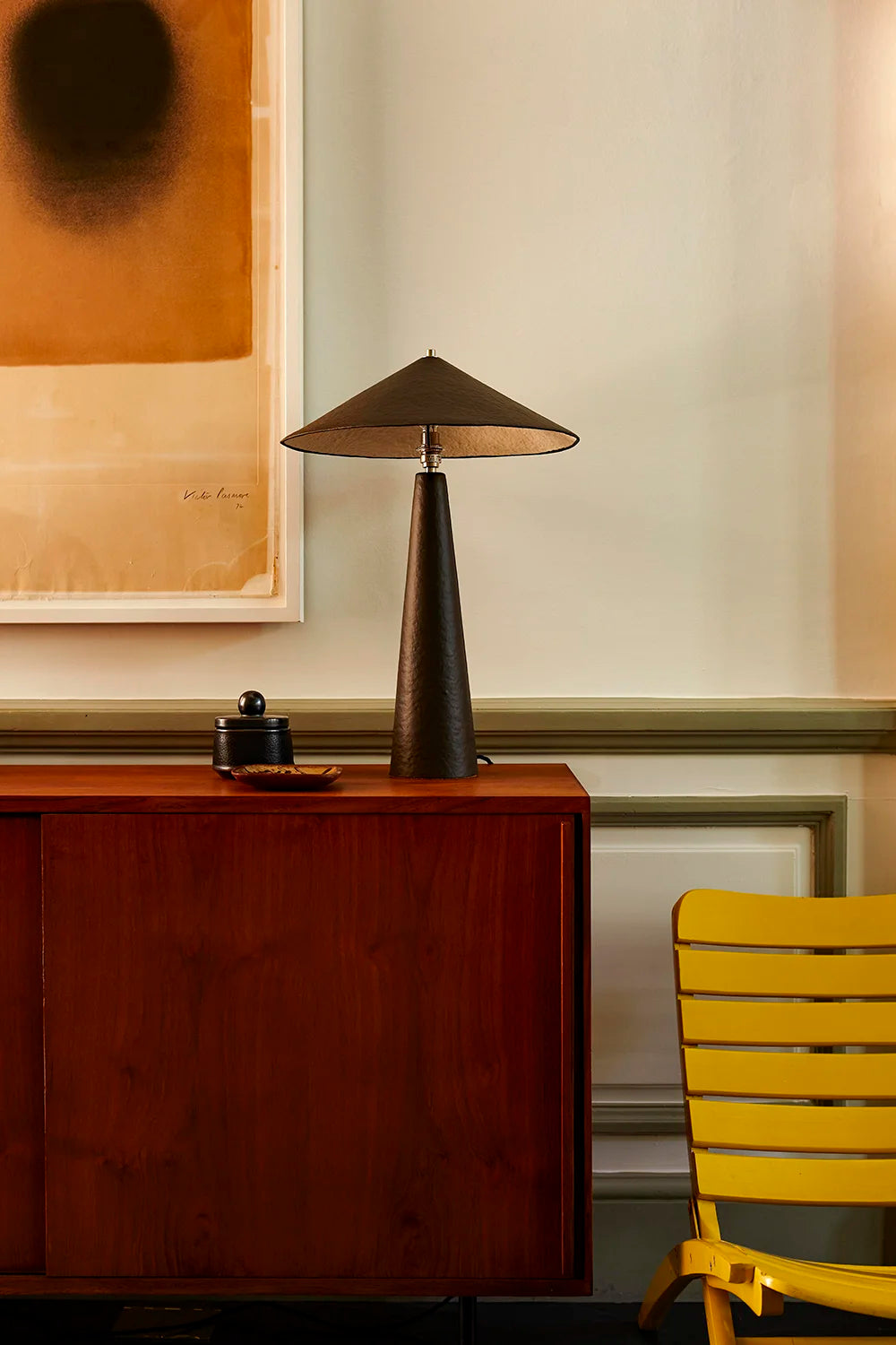 Table lamp on a wooden sideboard with a yellow chair and abstract art in the background