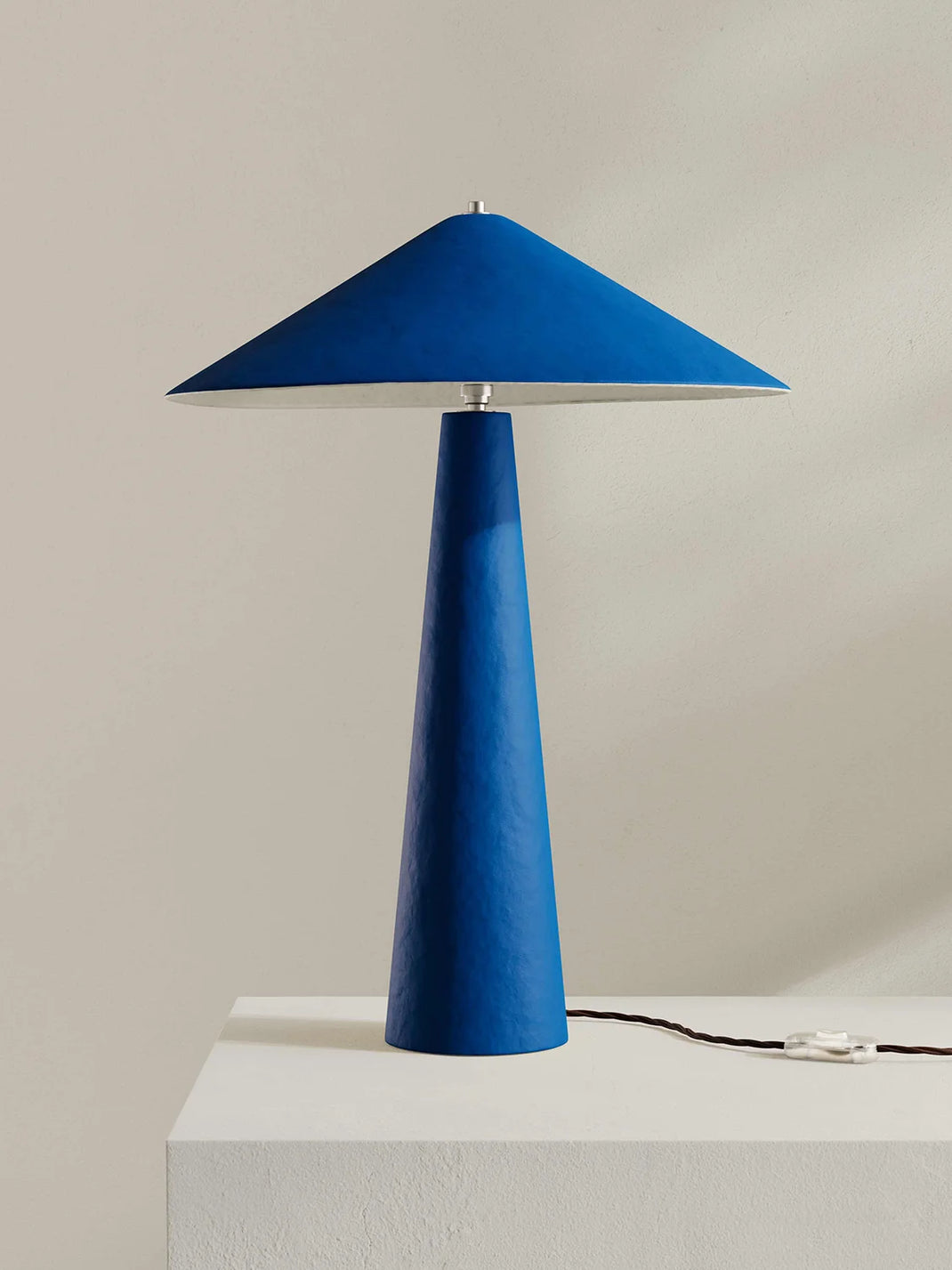 Blue table lamp with a conical base and rectangular shade on a light gray surface.