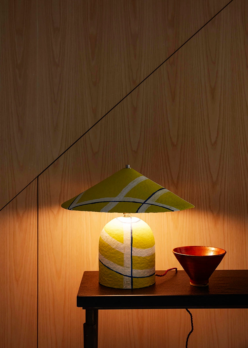 Yellow table lamp with a geometric, white striped shade on a wooden surface.