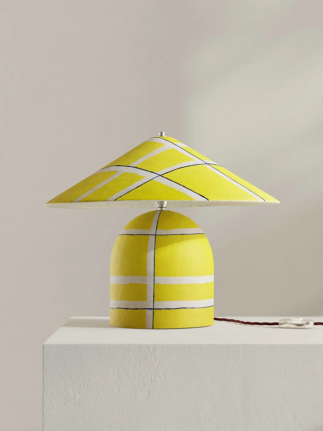 Yellow table lamp with striped design on a white surface against a beige background