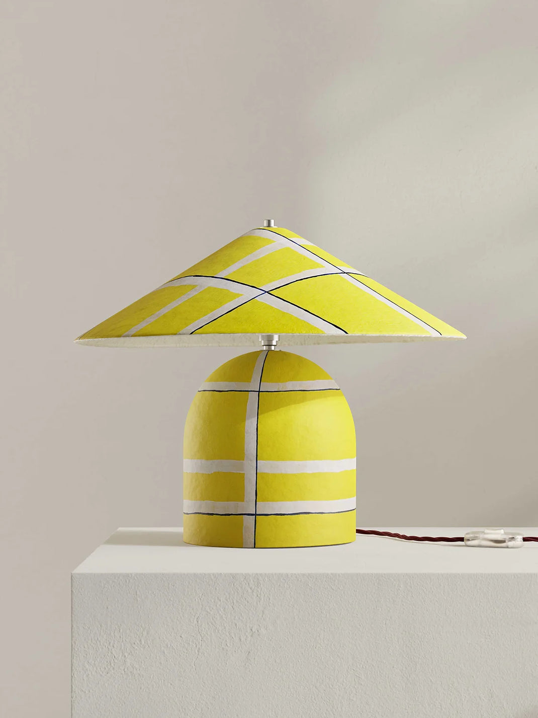 Yellow table lamp with striped design on a white surface against a beige background