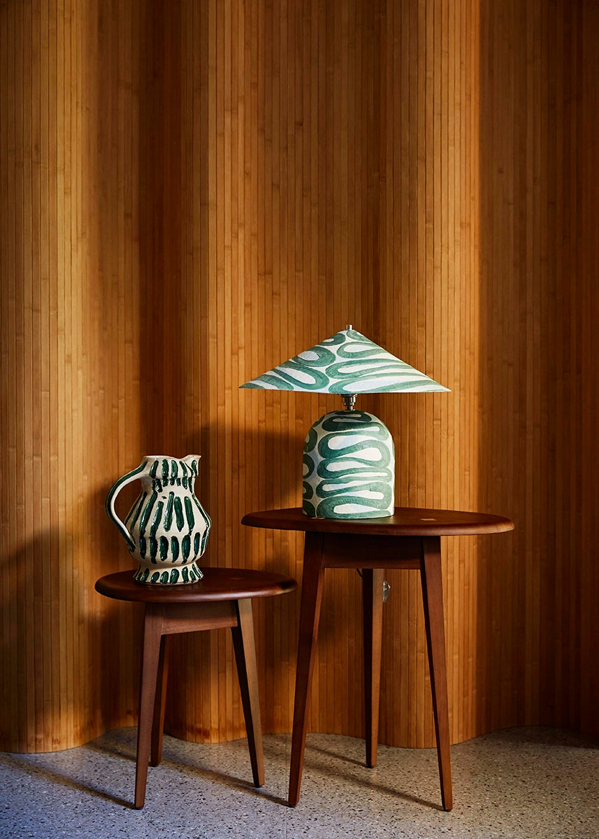 Two wooden side tables with a decorative table lamp and vase against a wooden paneled wall.