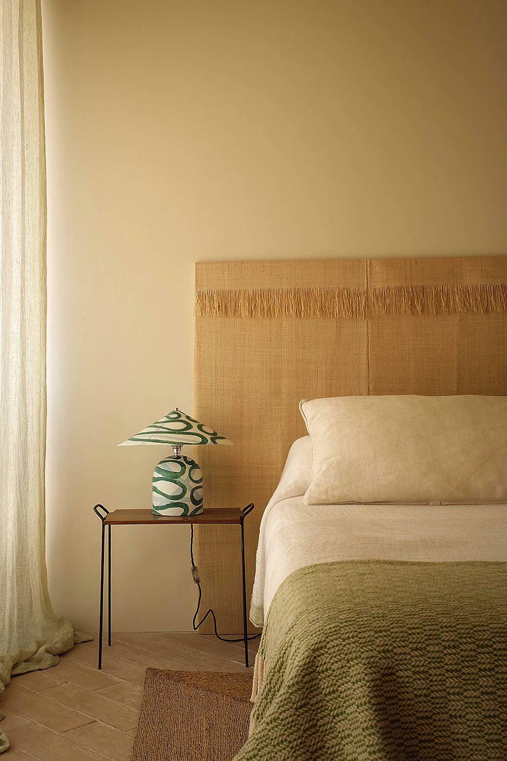 Bedroom with a bed, nightstand, and lamp against a beige wall.