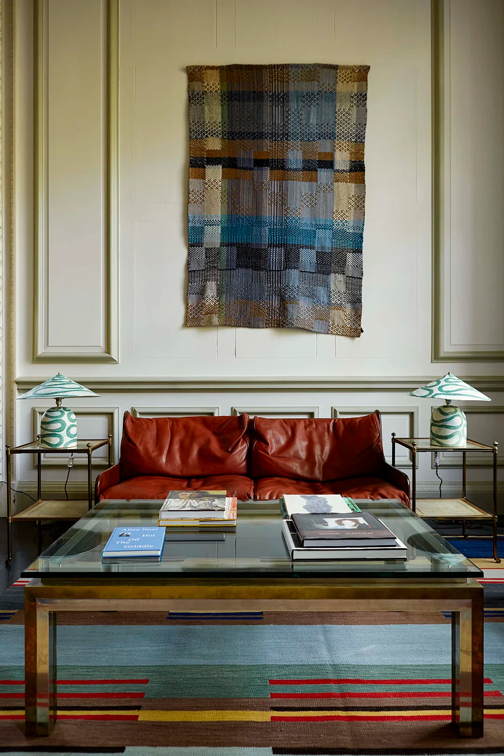 Living room with red sofa, glass coffee table, a serpent patterned table lamp on each end of the sofa and colorful wall tapestry.