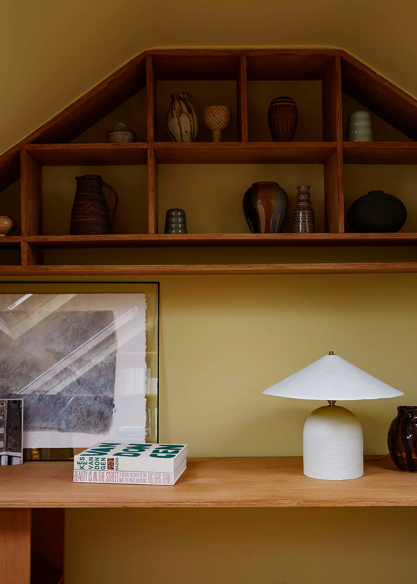 Wooden shelf with decorative items against a green wall, featuring a lamp and framed picture.