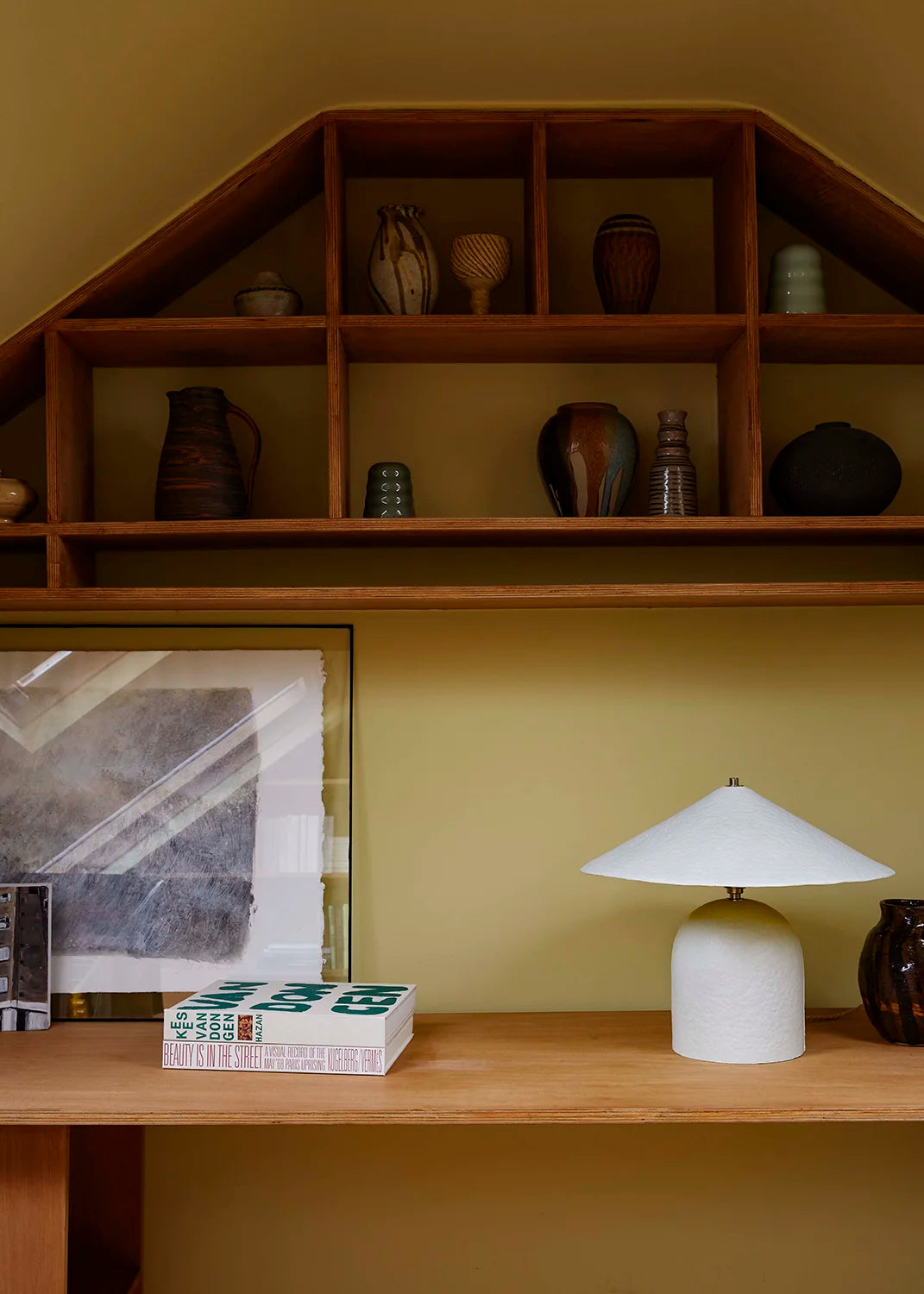 Wooden shelf with decorative items against a green wall, featuring a lamp and framed picture.