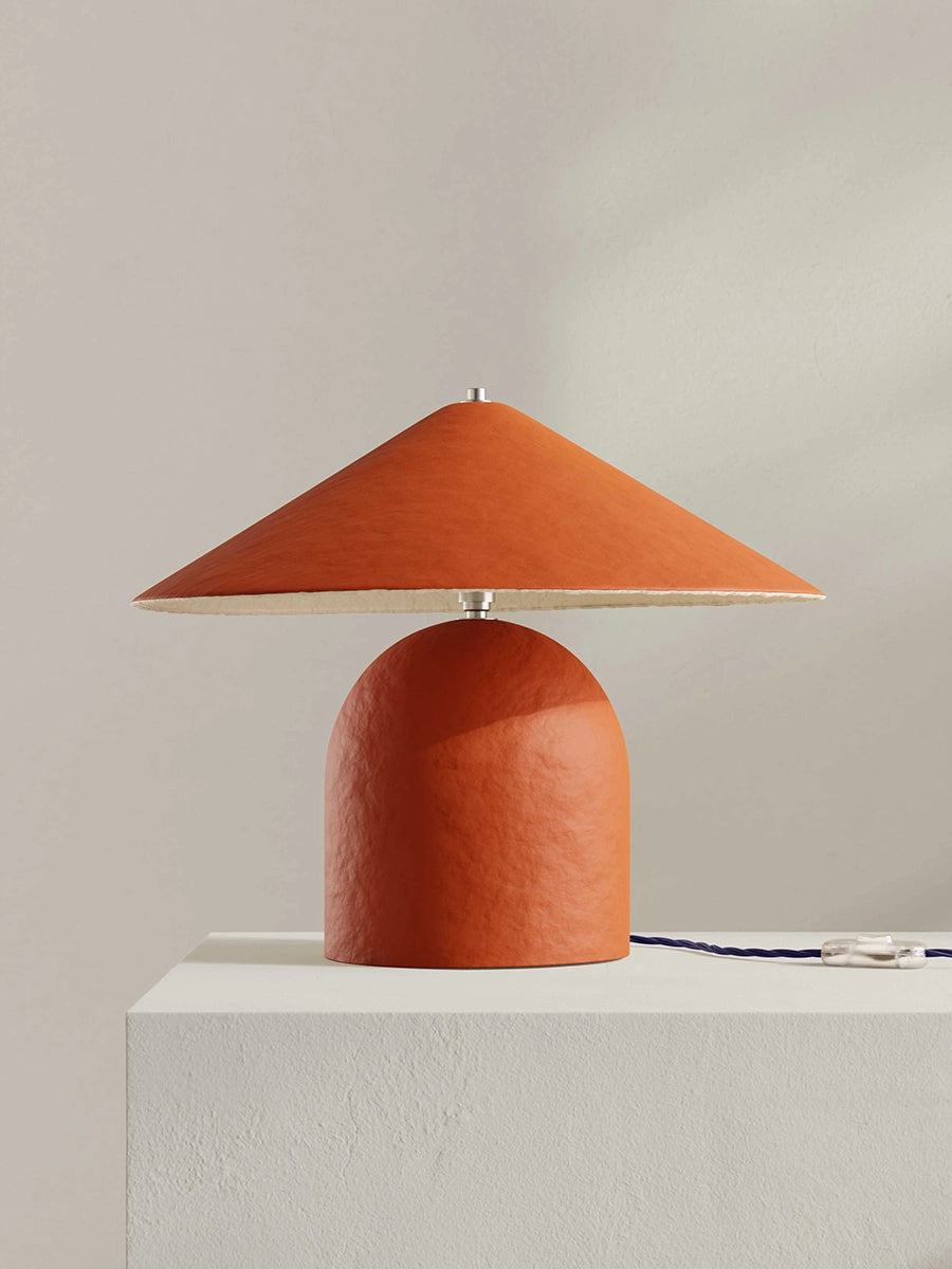 Orange table lamp with a textured shade on a white surface against a beige background