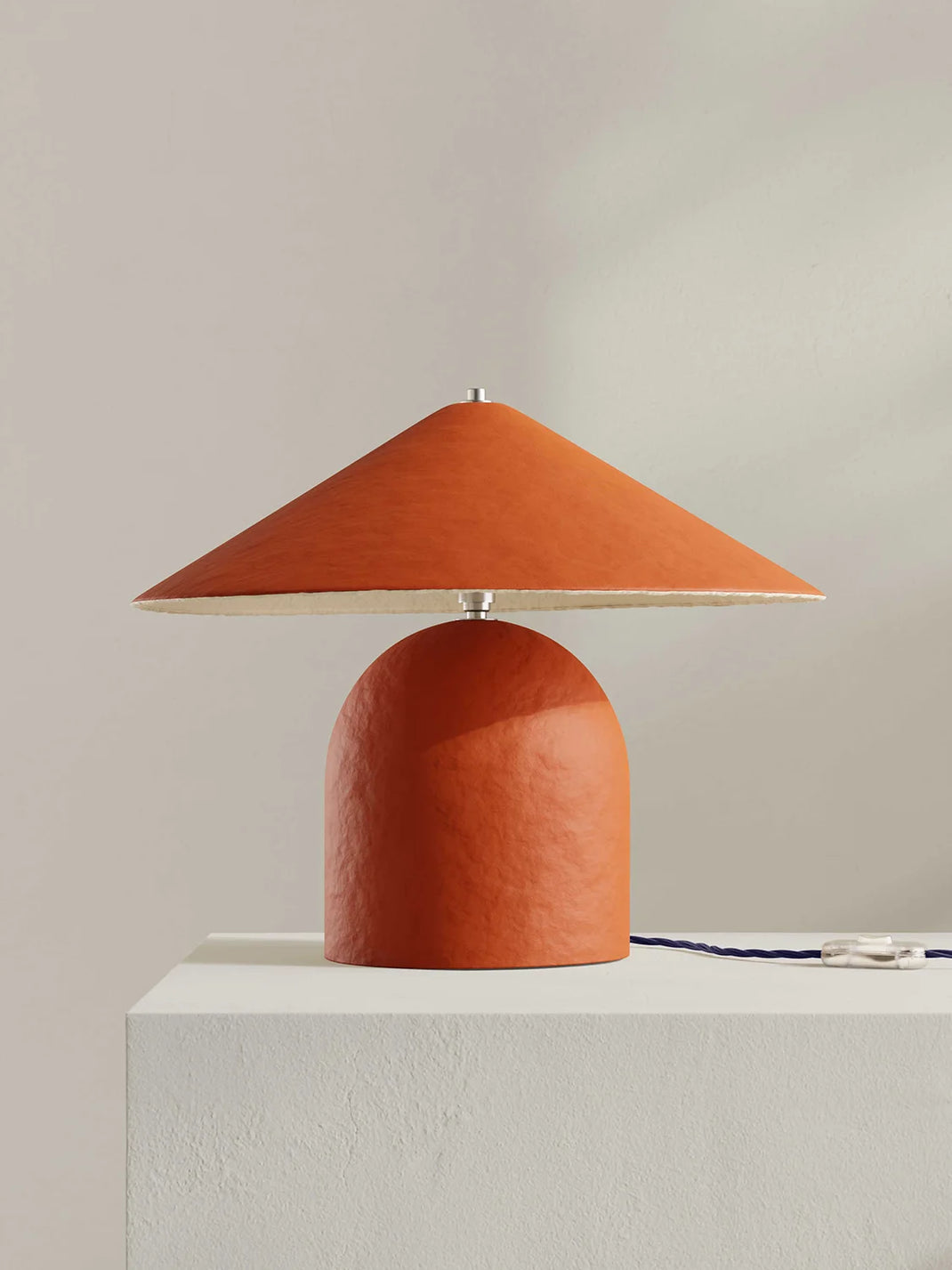 Orange table lamp with a textured shade on a white surface against a beige background