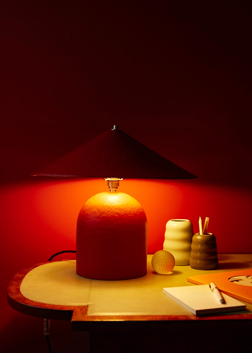 Desk with lamp and stationery against a dark red wall